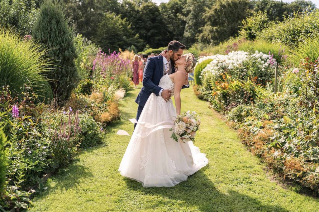 Sustainable Wedding Venues & Suppliers Leading the Way Bride and groom kiss on long borders in Homme House walled garden 4
